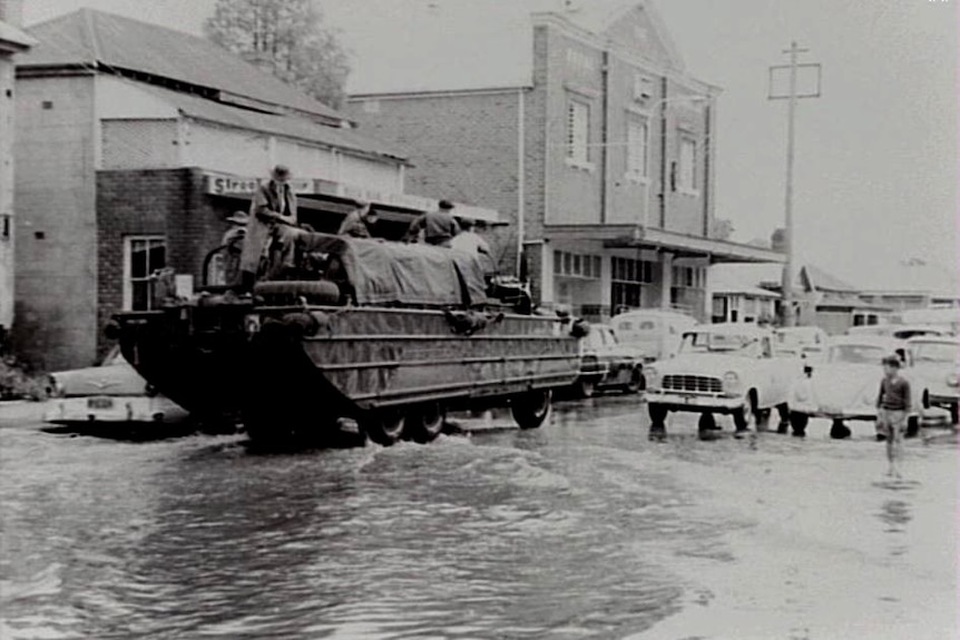 Des soldats dans un bateau à roues remontent une rue inondée.