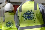 Two figures with hard hats and NBN vests look away from the camera