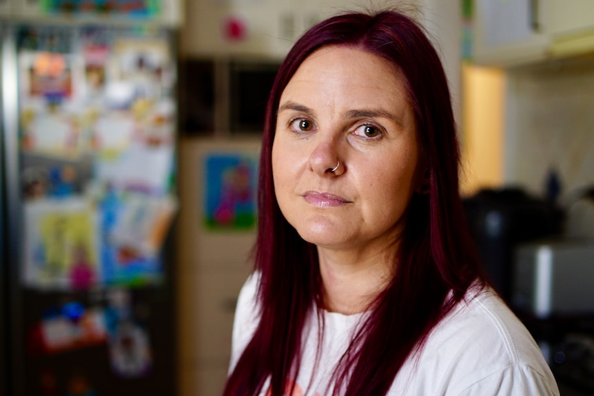 A women with dark red hair faces the camera with a somber expression on her face. 