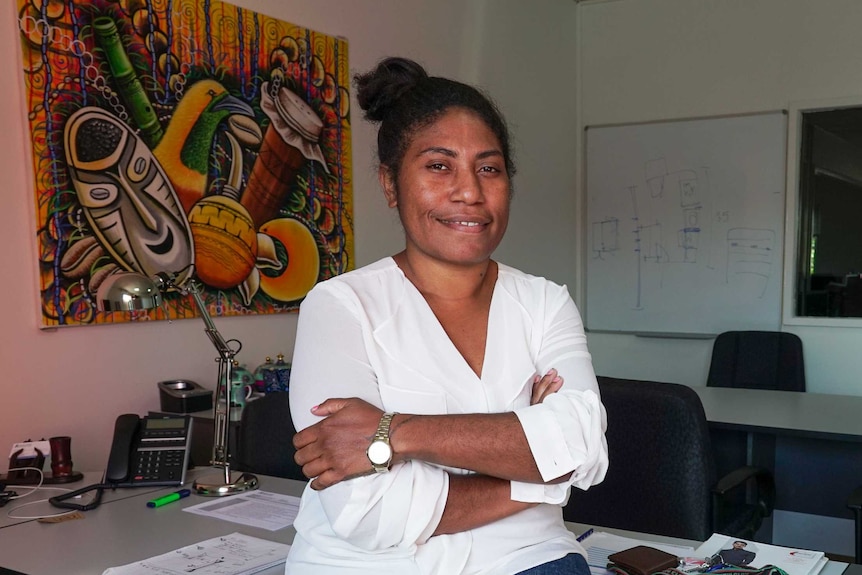 A Papua New Guinean woman leaning against her desk with her arms folded