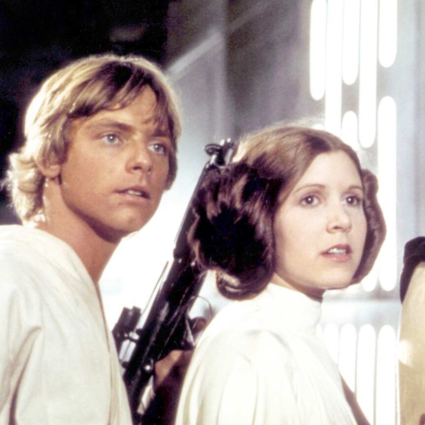 A still from the Star Wars Episode IV, featuring a close-up Luke Skywalker, Princess Leia and Han Solo creeping down a corridor.