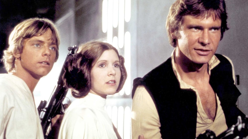 A still from the Star Wars Episode IV, featuring a close-up Luke Skywalker, Princess Leia and Han Solo creeping down a corridor.