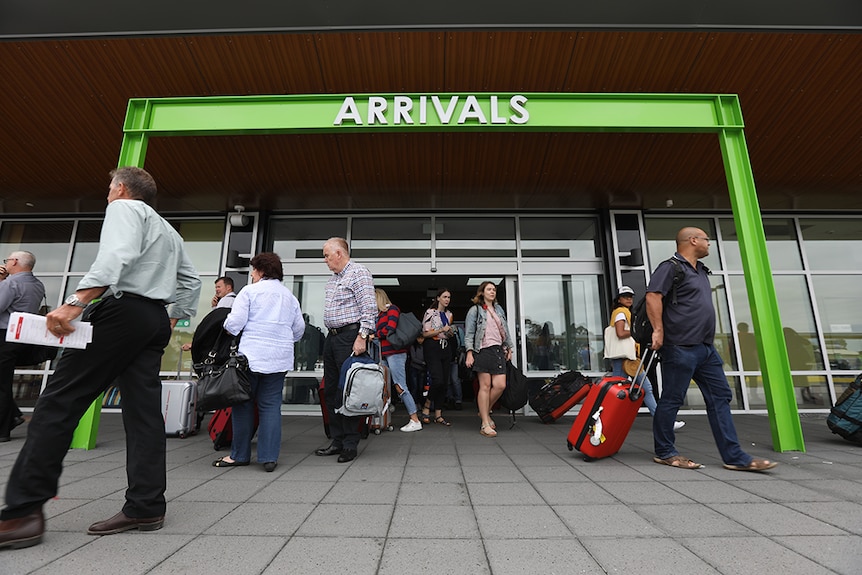 People walk under the arrivals sign at Hobart Airport