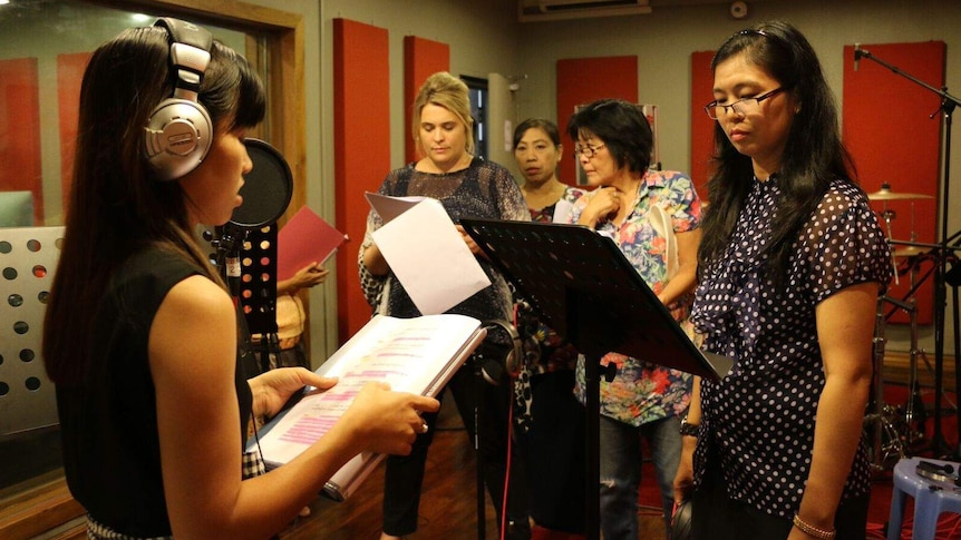 women standing in a audio studio reading from scripts