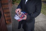 A person holding a pile of flyers, standing outside a residential mailbox.
