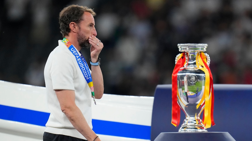 Gareth Southgate walks past a trophy and holds his mouth