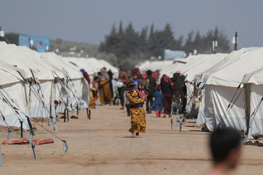 A girl walks as she carries a child past tents erected for the internally displaced following an earthquake.