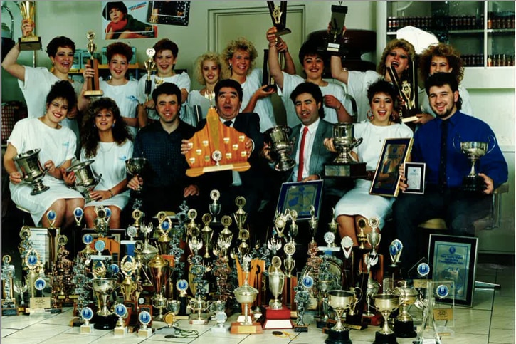 Cataldo’s Salon team with their competition trophies, circa 1980s. Front row 3rd from left: Emilio Cataldo, Giuseppe Cataldo, Angelo Cataldo, Anna Cataldo  Back row 5th from left: Karen Spradau (business partner and Director of Cataldo’s Salon Woden)