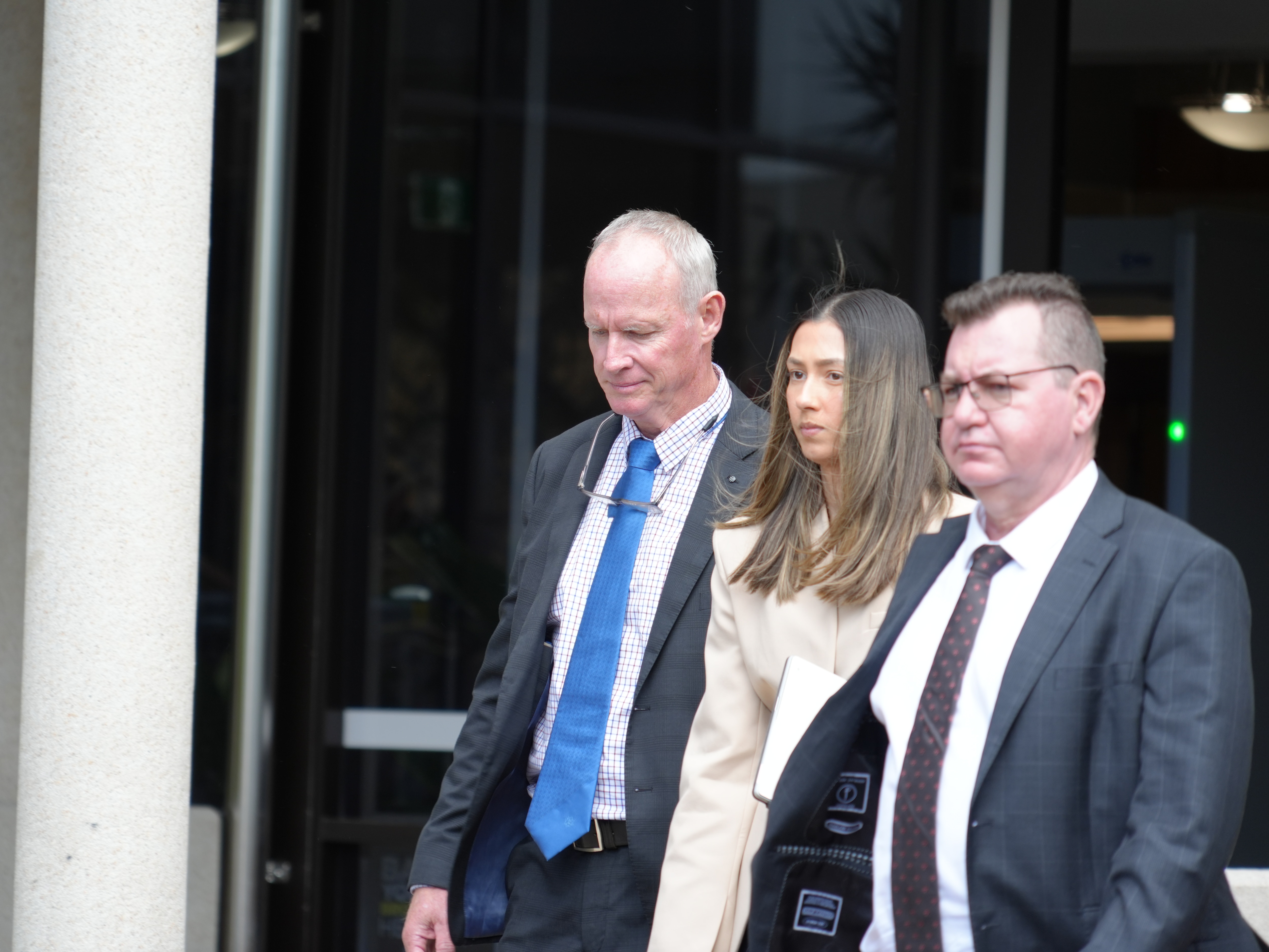 a man in blue tie and suit walks out of a courthouse with several other lawyers