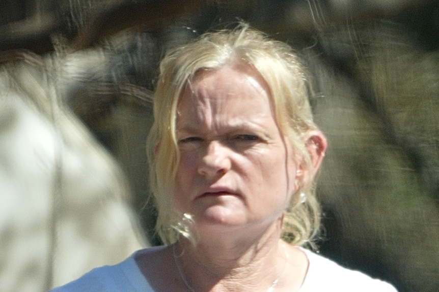 A woman with blonde hair and a white shirt looking angry.