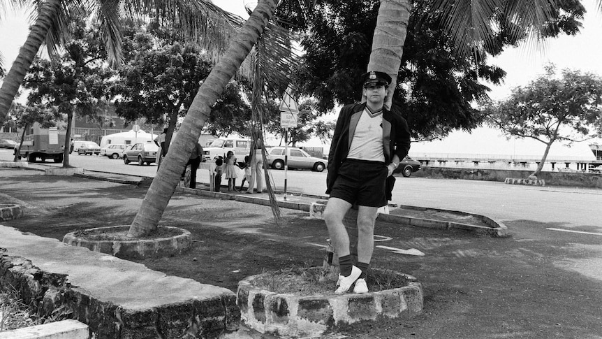 a black and white picture of Elton John leaning against a palm tree in Montserrat in the late 1980s