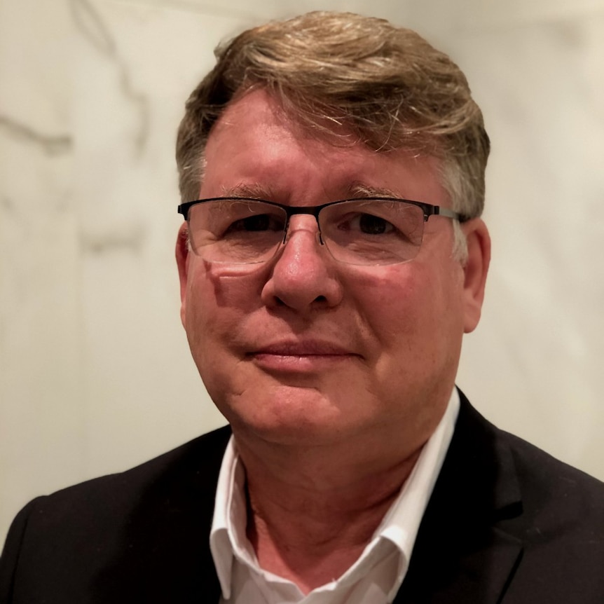 A tight headshot of a man with light coloured hair and spectacles on.