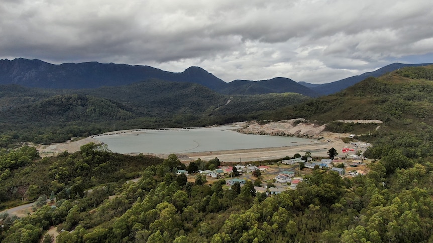 A dam, surrounded by bush and hills. Next to the dam are a few streets of houses.