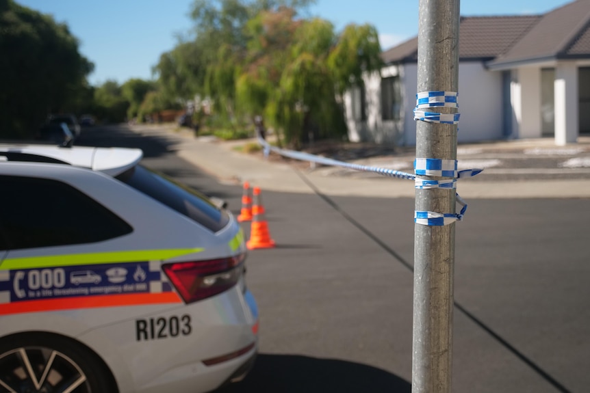 The rear of a police car parked near a pole holding up police tape in a suburban street.