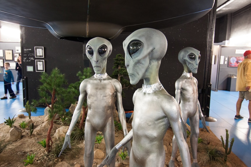 Three sculptures of green aliens with large black eyes in a museum 