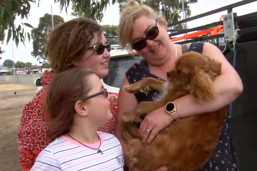 Shannon Hutchings holds the family dog as two of her daughters look on.