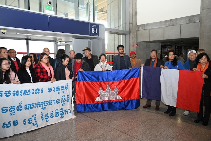 A group of people hold Cambodian and French flags at an airport corridor in Paris.