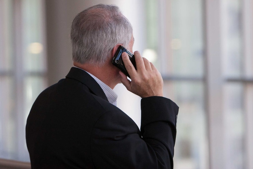 A man in a suit with grey hair looks away from the camera while holing a phone to his ear.