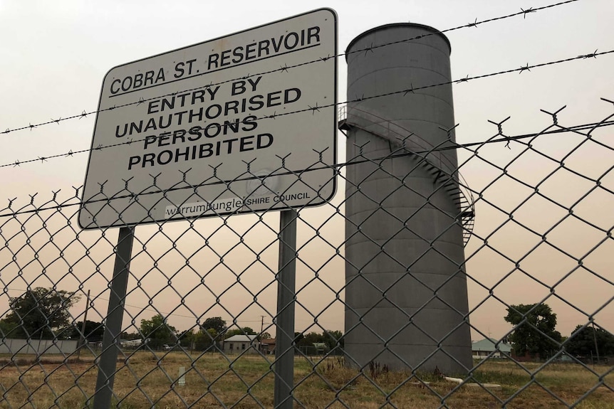 A picture of a water reservoir seen from outside a barbed-wire fence.