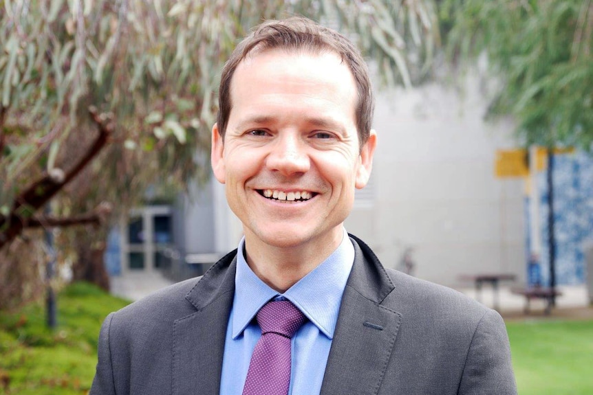 Associate Professor Matt Byrne stands, smiling on ECU's campus with trees in the background.