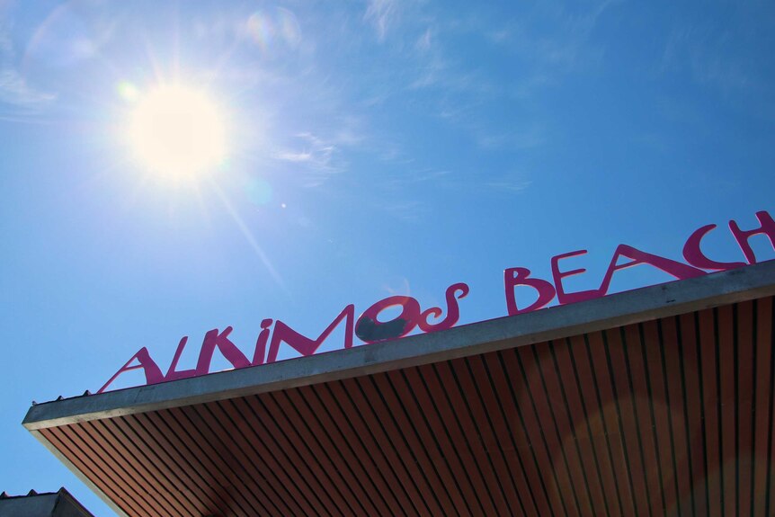 An Alkimos Beach sign on a building with the sun shining in the background.