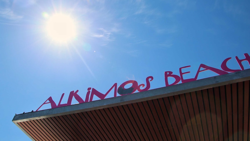 An Alkimos Beach sign on a building with the sun shining in the background.