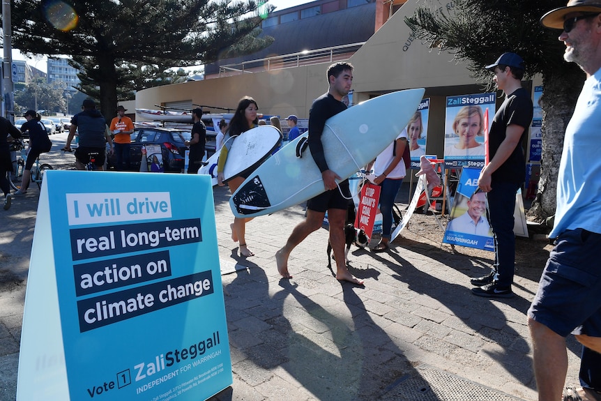 people carrying surfboards walking past voting booths