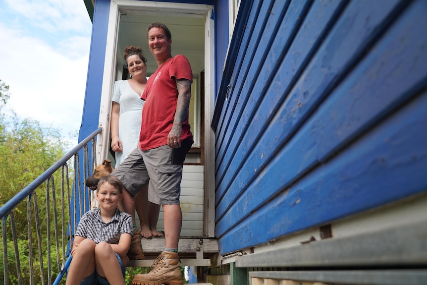 A woman and a man stand on a staircase, while a boy and a dog sit on the steps