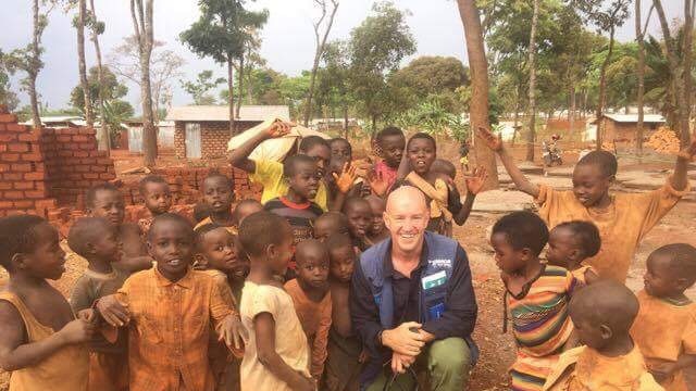Andrew Harper kneels in an African village, surrounded by 15-20 local children
