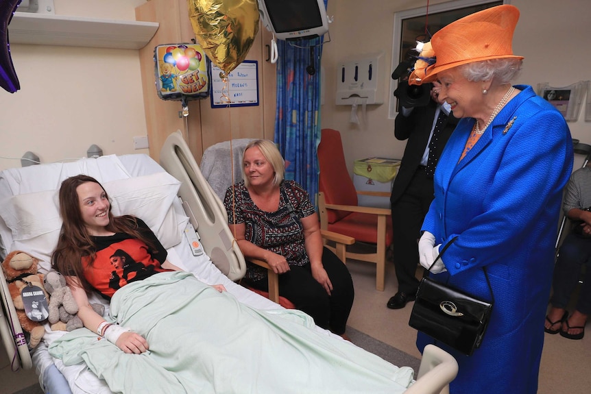 Queen Elizabeth II speaks to a girl lying in a hospital bed.