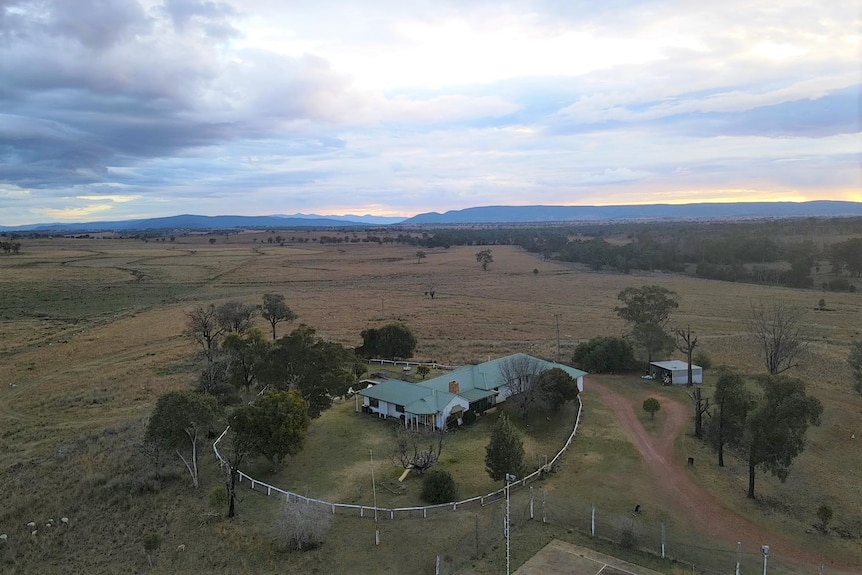 An aerial view of a farm, with a large house with a green roof. 