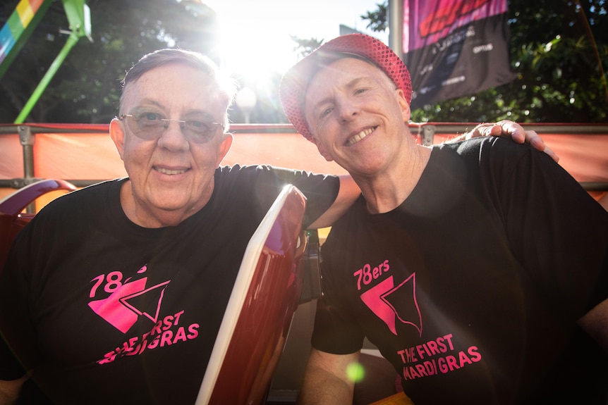 Deux hommes aux cheveux grisonnants vêtus de t-shirts noirs des 78ers sourient à la caméra