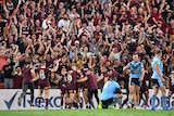 Players hug and celebrate near the sidelines in front of a large crowd with their hands in the air