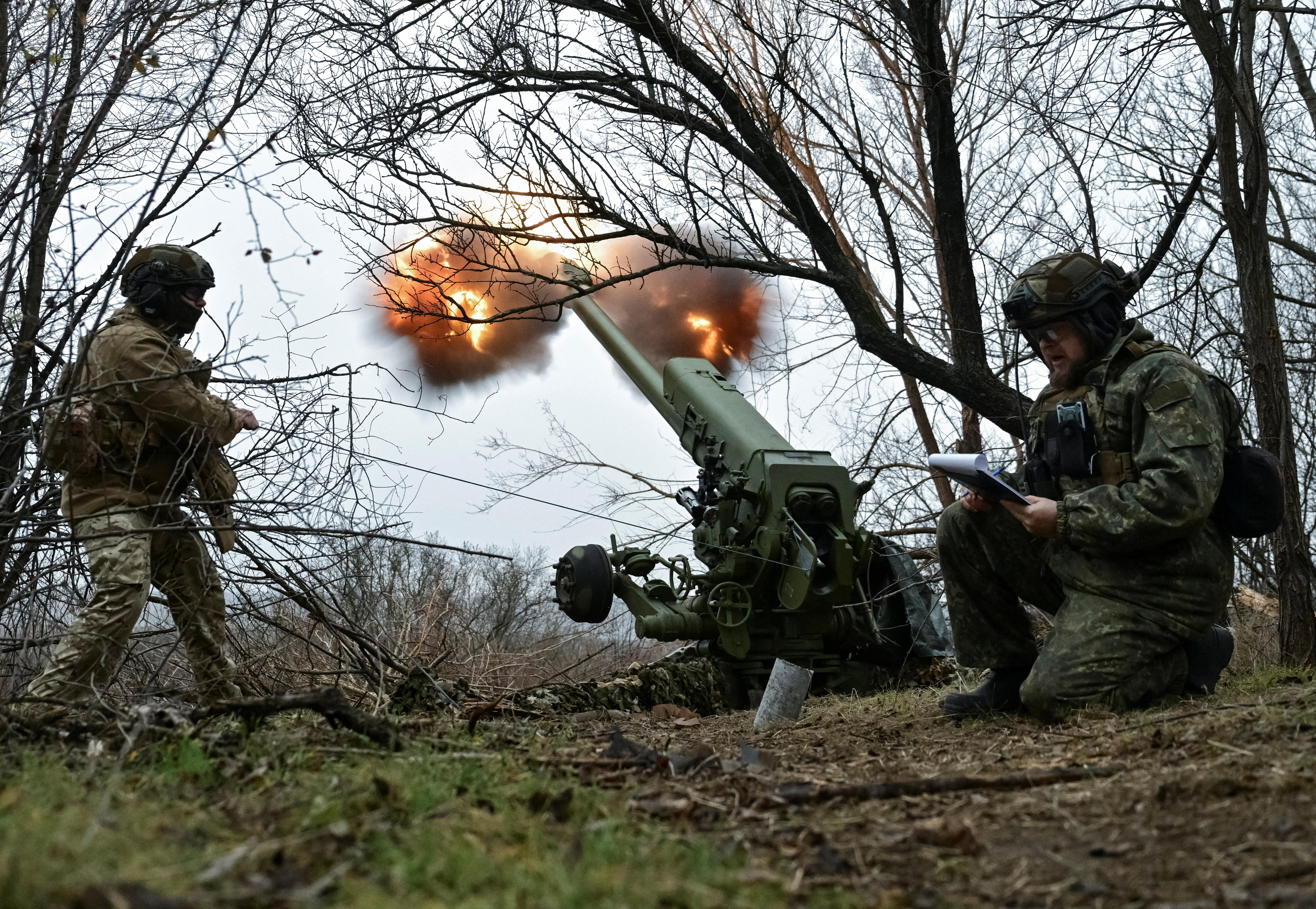 Ukrainian soldiers standing next to a firing Howitzer artillery gun.