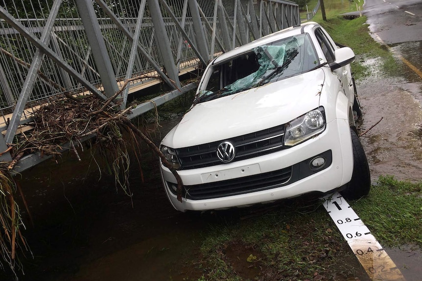 A car with a windscreen smashed after it washed off the road and into a footbridge