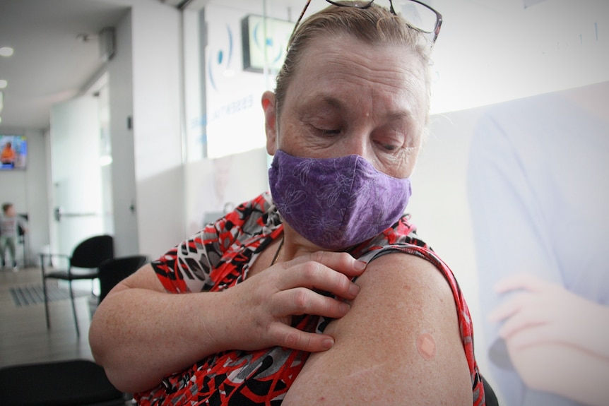 a woman in a mask looking a bandaid where she got a needle shot