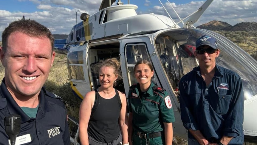 A woman stands with three people in front of a helicopter - two are in police and paramedic uniforms. 