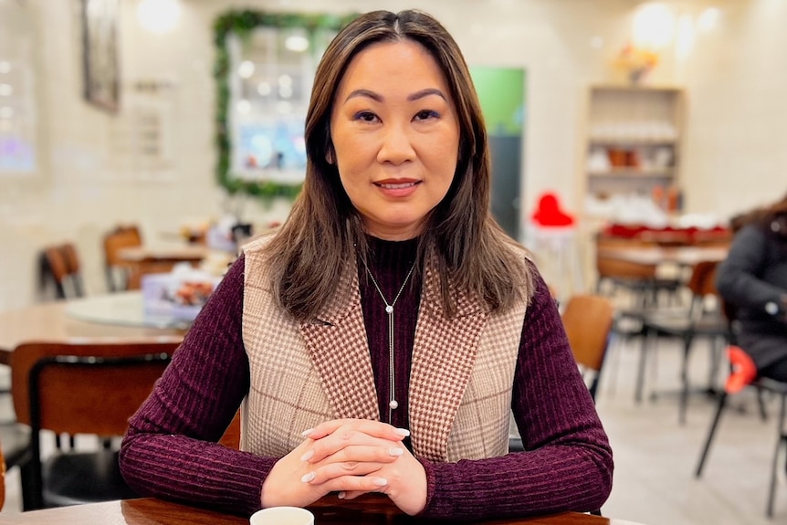 A woman sits at a table and smiles at the camera.