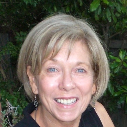 Colleen Ryan smiling in front of green foliage.