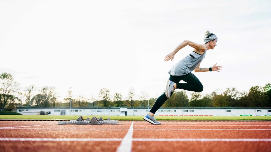 Solo woman sprinter, training, taking off from starting blocks on an athletics track