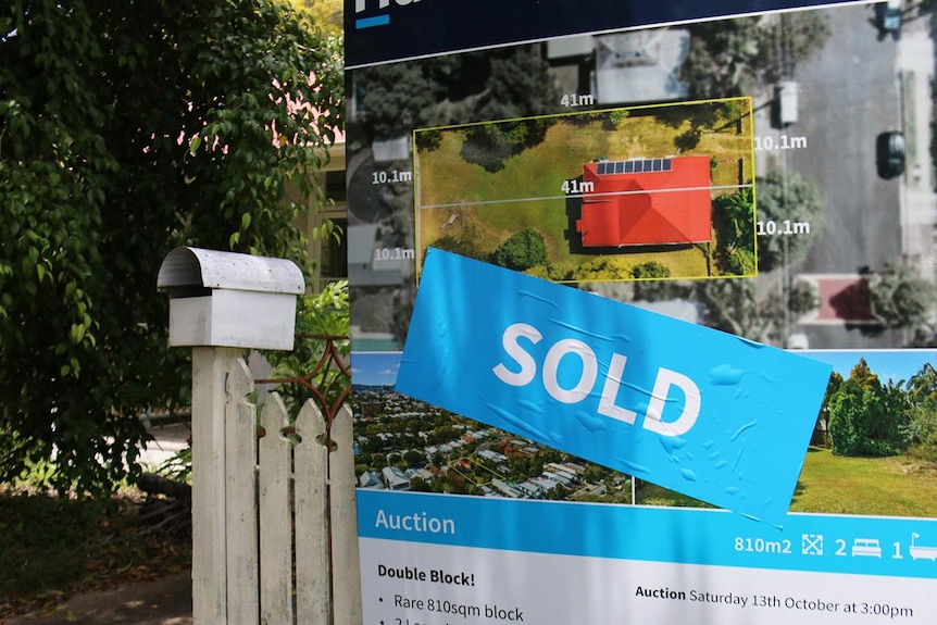 Sold sign next to letterbox and fence of Queenslander-style house.