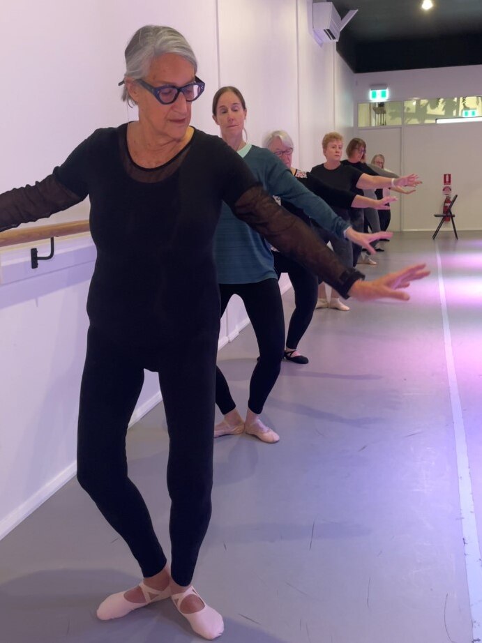 A row of women at the barre bend their knees outward with their heels together. 