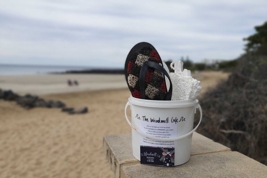 A white bucket full of rubbish, including a thong, with the beach in the background
