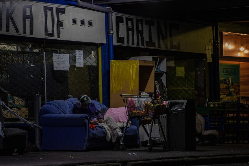 A woman sleeps out the front of the drop-in centre with 'Waka of Caring' written on the wall