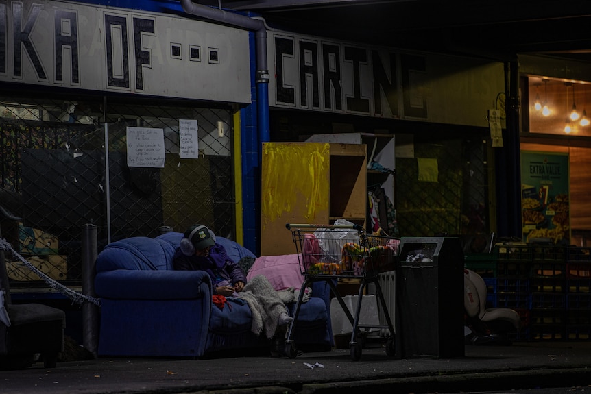 A woman sleeps out the front of the drop-in centre with 'Waka of Caring' written on the wall