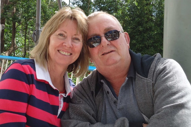 A woman in striped top and a man in sungalsses post for a photo, smiling with a tree-lined background