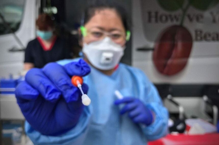 A person in full PPE gear holds out a swab to the camera