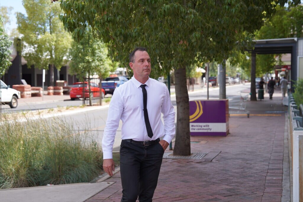 Hombre con camisa blanca y corbata negra camina con una mano en el bolsillo 