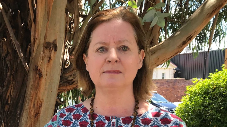 a woman stands in front of a large gum tree.