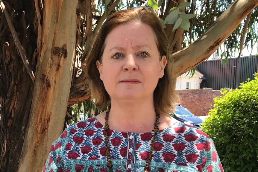 a woman stands in front of a large gum tree.